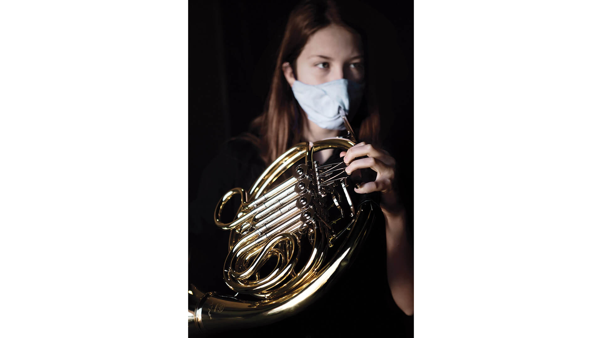 Masked student holds French horn with bell cover