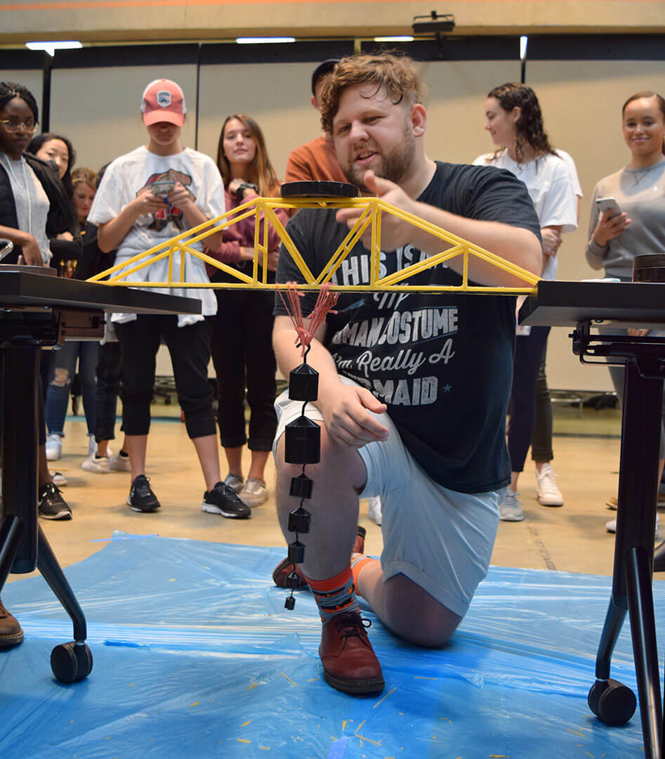 Student applies weights to pasta bridge