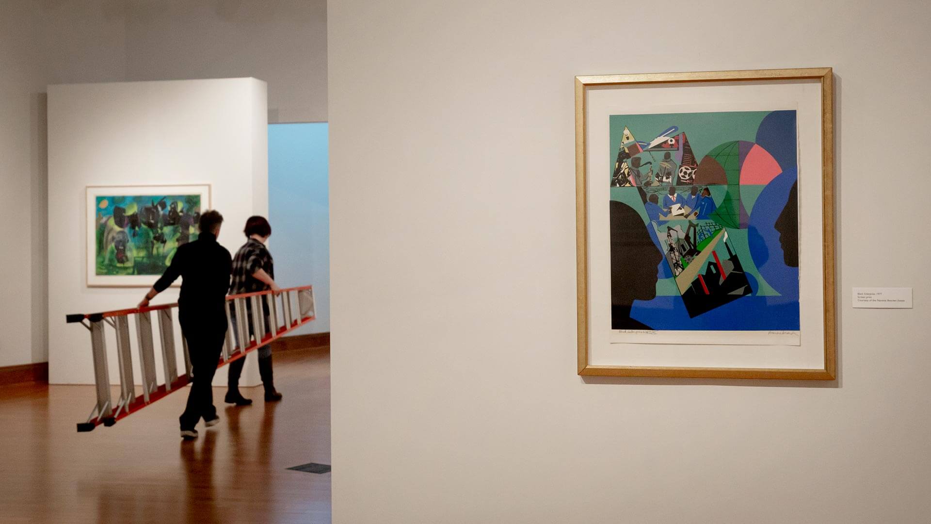 Two people carry a ladder in an art gallery