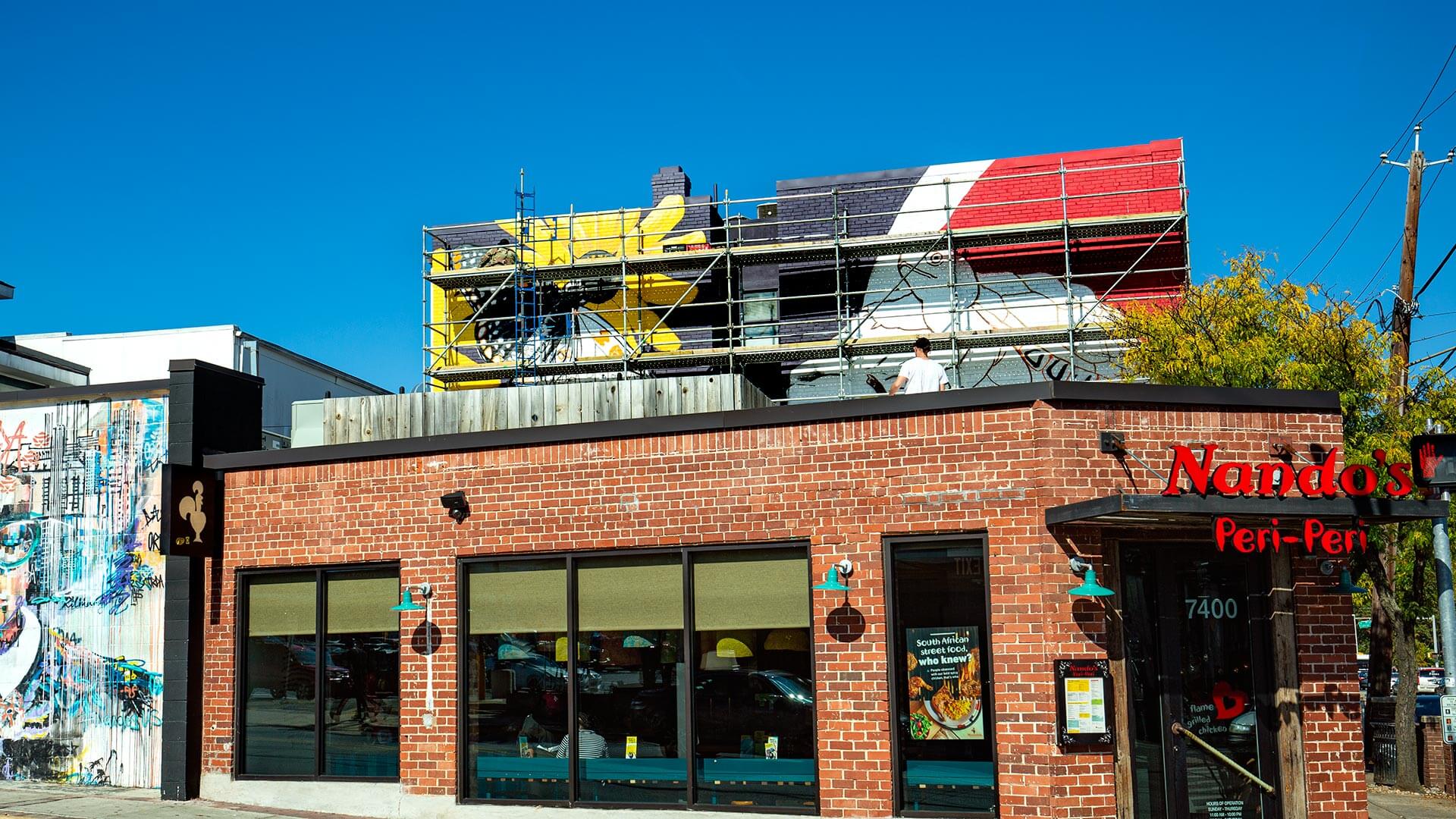 Mural on brick wall above Nando's Peri-Peri showing a yellow flower and a terrapin outline on a red, black and white background